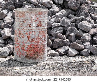 Old and dirty empty red and gray oil drum barrel and large gray stone pile in background