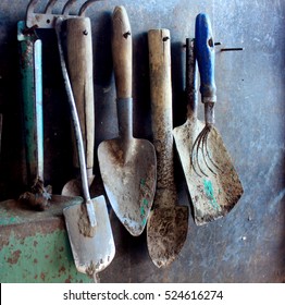 Old Dirty Farm Metal Garden Tools As Shovels And Rakes Hanging On The Wall On Nails