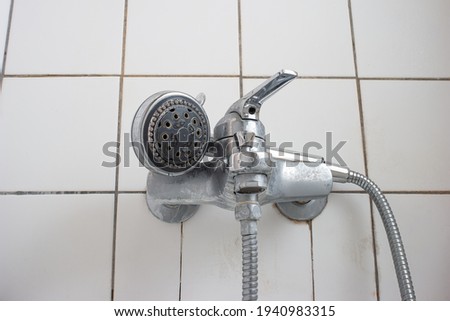 Old dirty limescale chalk covered shower head and bathtub faucet close up low angle view.