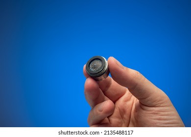 Old Dirty Limescale Covered Clogged Up Tap Water Faucet Strainer Or Aerator Held In Hand By Caucasian Male. Close Up Studio Shot, Isolated On Blue Background.