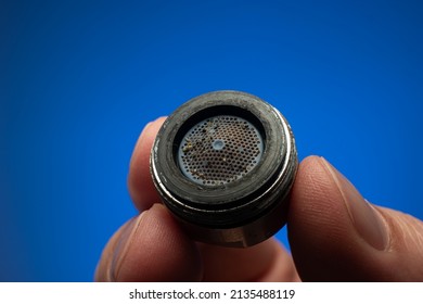 Old Dirty Limescale Covered Clogged Up Tap Water Faucet Strainer Or Aerator Held In Hand By Caucasian Male. Close Up Studio Shot, Isolated On Blue Background.