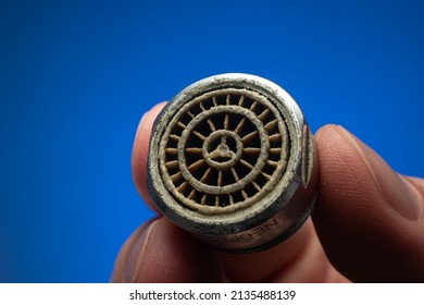 Old Dirty Limescale Covered Clogged Up Tap Water Faucet Strainer Or Aerator Held In Hand By Caucasian Male. Close Up Studio Shot, Isolated On Blue Background.