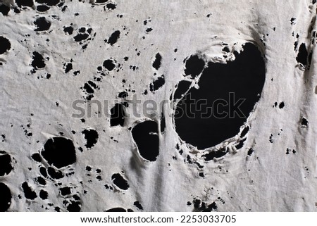old dirty ragged shirt with holes, grunge damaged cloth on black background, ripped white fabric with many holes