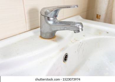Old dirty washbasin with rust stains, limescale and soap stains in the bathroom with a faucet, water tap.
