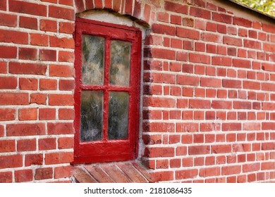 Old Dirty Window In A Red Brick House Or Home. Ancient Casement With Red Wood Frame On A Historic Building With Clumpy Paint Texture. Exterior Details Of A Windowsill In A Traditional Town Or Village