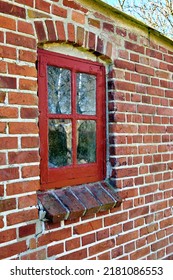 Old Dirty Window In A Red Brick Home. Ancient Casement With Red Wood Frame In A Historic Building With Lumpy Paint Texture. Exterior Details Of A Windowsill In A Traditional Town Or Village