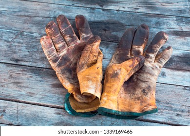 Old Dirty Work Gloves On A Wooden Table Stained With Grease And Oil. Hard Work Professions Are Not Always Well Rewarded