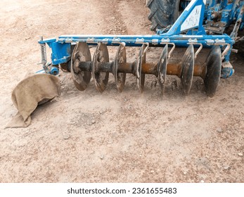The old disc harrow behind the large tractor after till the land in the farm, front view with the copy space. - Shutterstock ID 2361655483