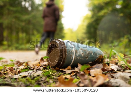 Old disposable coffee cup in the forest next to the road with person in a background. Plastic recycling, pollution and global warming theme. Take away food industries impact on the environments. 