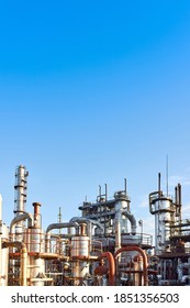 Old Distillation Column Towers And Reactors Under Blue Evening Sky Background At Chemical Plant. Exterior Of Silver Metal Rusty Enterprise Vertical With Copyspace.