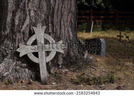 An old disused wooden cross set against a pine tree at Hawridge Church graveyard, Buckinghamshire, England.