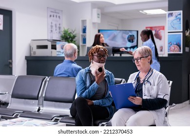 Old Doctor Consulting Woman At Facility, Wearing Cervical Neck Collar To Cure Injury And Pain. Specialist And Patient With Medical Foam Brace Talking About Recovery In Waiting Room At Health Center.