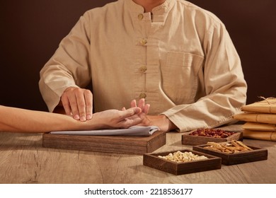 The old doctor of traditional Chinese medicine to the patient's pulse with wooden tray of herbs medicine next to.

 - Shutterstock ID 2218536177