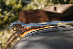 An Old Dodge Truck Hood Ornament, The Iconic Ram.  Reflected In The Ram Hood Ornament Is An Old Red And Yellow Shell Gasoline Truck From The 1950's.
