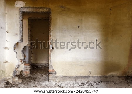 Old doorway in a dilapidated damaged brick building with debris strewn across the floor and dingy yellow walls as an architectural background