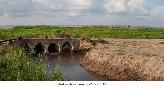 Old drainage culvert structure spanning shallow water channel in rural wetland near horizon sea, South Ukraine