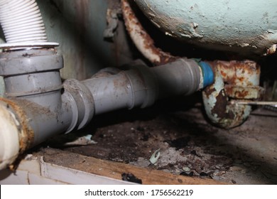 Old Drainage Pipeline From The Bathroom With Gray Plastic And Rusty Metal Pipes With Blue Duct Tape To Repair The Plumbing In The Bathroom