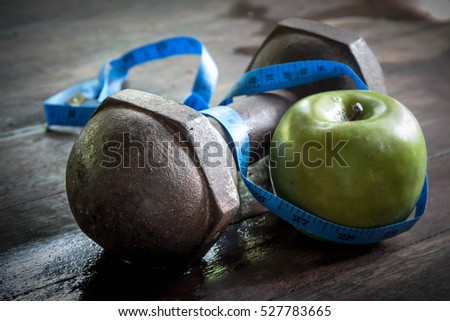 Old dumbbell with green apple and  measuring tape on wooden table,Sport equipment,Healthy lifestyle concept,Still life photography