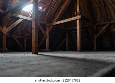 Old Dusty Attic Of A Building. Empty Space Lit By A Roof Window. Wooden Construction Of The Roof. Spooky Place In A Big House With A Horror Atmosphere.