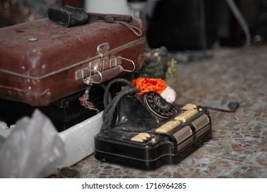 An old, dusty, black telephone from the mid-20th century and a tattered suitcase on the stone floor among old things and garbage