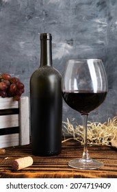 Old dusty bottle of wine and glass on wooden table against gray wall