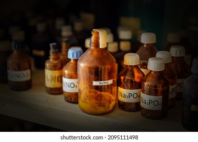 Old dusty bottles with chemicals on a shelf in the science classroom. Substances for experiments in dark glass bottles with inscriptions, close-up. Concept of school education.