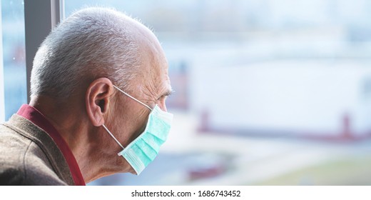 Old Elderly Man In Protective Face Mask Against Virus Looks Out Through Window Stay At Home For Health Safety