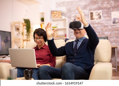 Old Elderly Retired Man Using VR Virtual Reality Headset In Their Cozy Apartment.