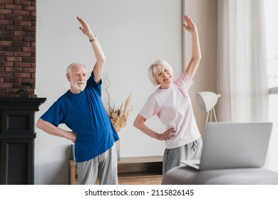 Old Elderly Senior Grandparents Spouses Couple Husband And Wife Doing Sports Activity Using Laptop Online Tutorial On Home Fitness. Shaping, Keeping Fit, Doing Yoga Exercise Training On Lockdown