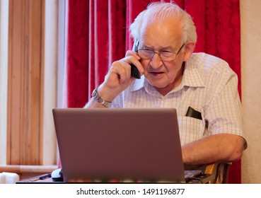 Old Elderly Senior Man On Phone At Laptop Computer At Risk To Cyber Attack And Online Bank Fraud
