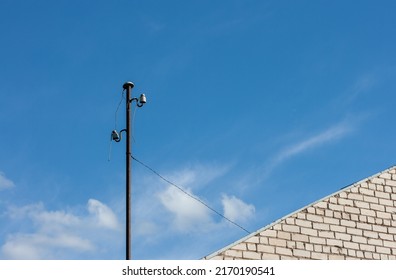 An Old Electric Metal Pole With Wires At The Corner Of The House On A Sunny Summer Day With A Blue Sky.