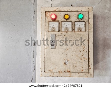 Old electrical control panel with indicator lights and analog meters mounted on a worn, rusty metal box, representing industrial infrastructure and vintage electrical equipment.