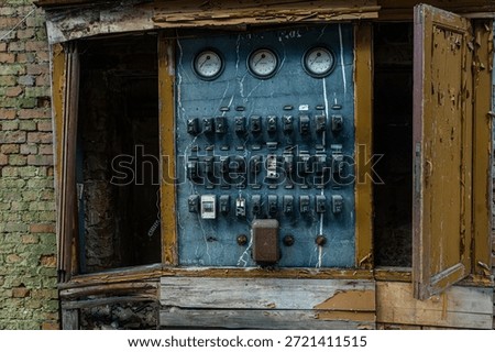 Old electrical control panel with switches meters and peeling paint inside a derelict industrial building