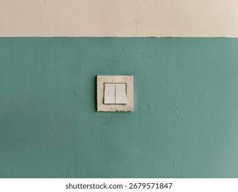 Old electrical socket and light switch on a green painted wall, showing signs of dirt and wear, suitable for background, texture, or utility concept.