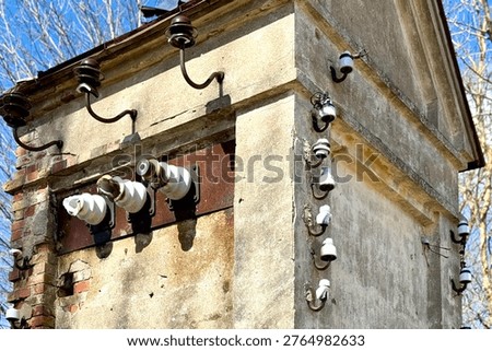 Old electrical transformer building with ceramic insulators and exposed wiring on weathered wall. Vintage industrial detail in outdoor setting.