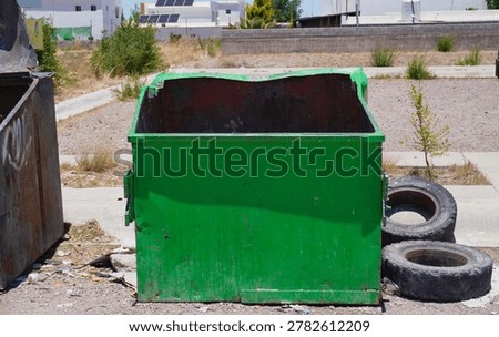 An old empty garbage container in bad conditions, placed near a street