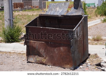 An old empty garbage container in bad conditions, placed near a street