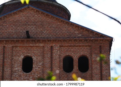 an old empty red brick building close by and blurred green leaves on branches in front