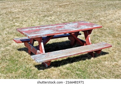 Old Empty Weathered Wood Picnic Table With Red Paint Peeling, On Dry Grass.