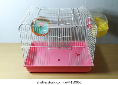 Old And Empty White And Pink Hamster Cage On Wood Desk With Hamster Wheel And Yellow Hamster Toilet