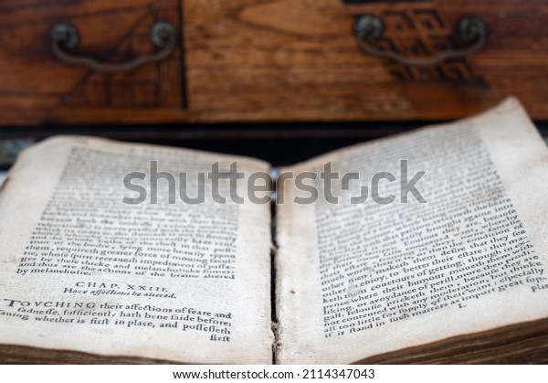 An Old English Book Lays\
Open In Front Of An Antique Jewelry Box. Most of the image is\
composed on the book, two columns of text, divided by a worn out\
spine of a book.