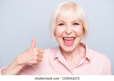 Old excited lady showing thumbs up gesture, laughing on grey background