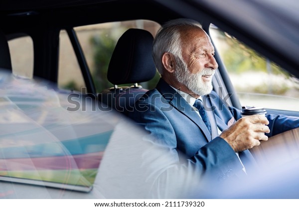 An old executive\
drinks coffee while driving a car. A happy senior businessman sits\
in his car and drives himself to work while finishing his morning\
takeaway coffee.