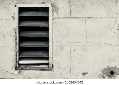 Old Exterior cinderblock cement wall with slat metal shuttered wood framed window in disrepair, grunge black and white mono with copy text space for background