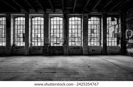 Old factory windows and worn wooden floorboards in run-down factory ruins in Germany. Typical metal window frames with some broken, very dirty panes. Black and white lost place with high contrast.