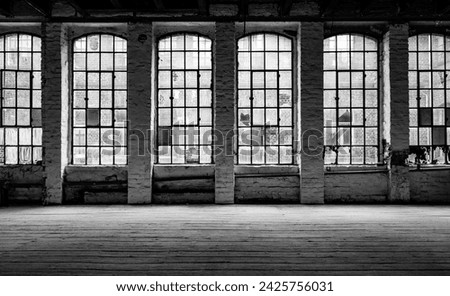 Old factory windows and worn wooden floorboards in run-down factory ruins in Germany. Typical metal window frames with some broken, very dirty panes. Black and white lost place with high contrast.
