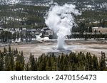 Old Faithful geyser with visitor center in background seen from observation point on Old Faithful Geyser Loop trail behind geyser at Yellowstone National Park