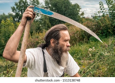 Old farmer rests on the field with scythe; agricultural and eco farming concept; autumn harvest wield a scythe; white beard ed old man outdoors. 