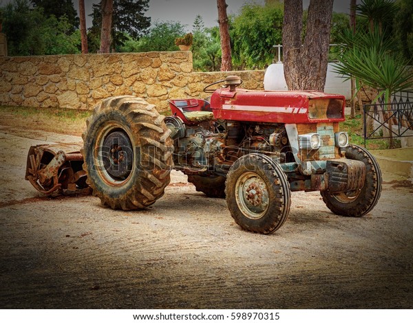 Old fashion antique worn rusted rural red four\
wheel tractor among green trees. Old agricultural industry machine\
crawler tractor farm vehicle. Abstract agricultural tractor rusted\
metal beast