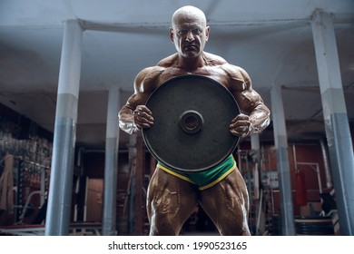 Old Fashion Athlete Bodybuilder Doing Arm Exercises In Gym. Brutal Bald Caucasian Sports Man Style Of The 80s. Sport, Fitness And Workout 80s Concept